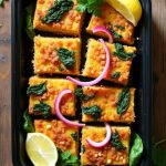 Baked Gluten-Free Chickpea Socca Slices with Spinach and Red Onions served with lemon wedges.